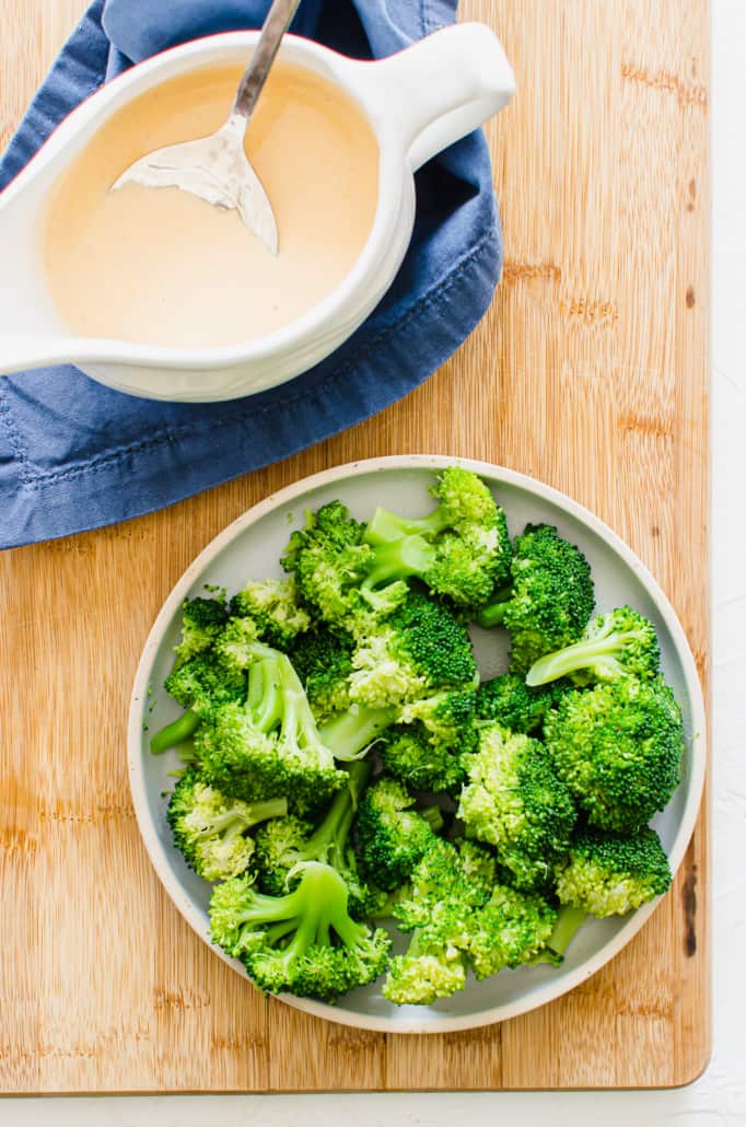 broccoli cheese sauce in a white serving bowl next to a plate of steamed broccoli