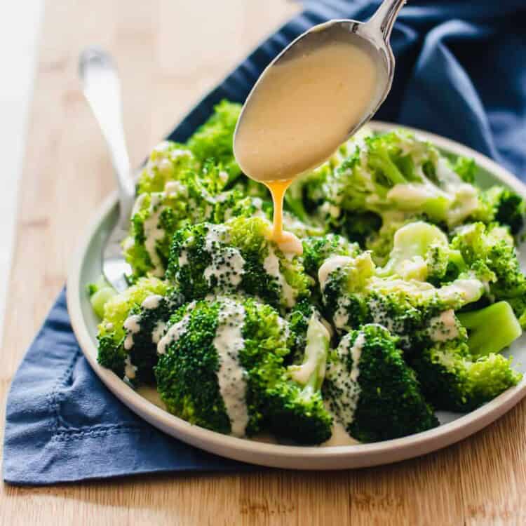 Homemade cheese sauce being spooned over steamed broccoli.