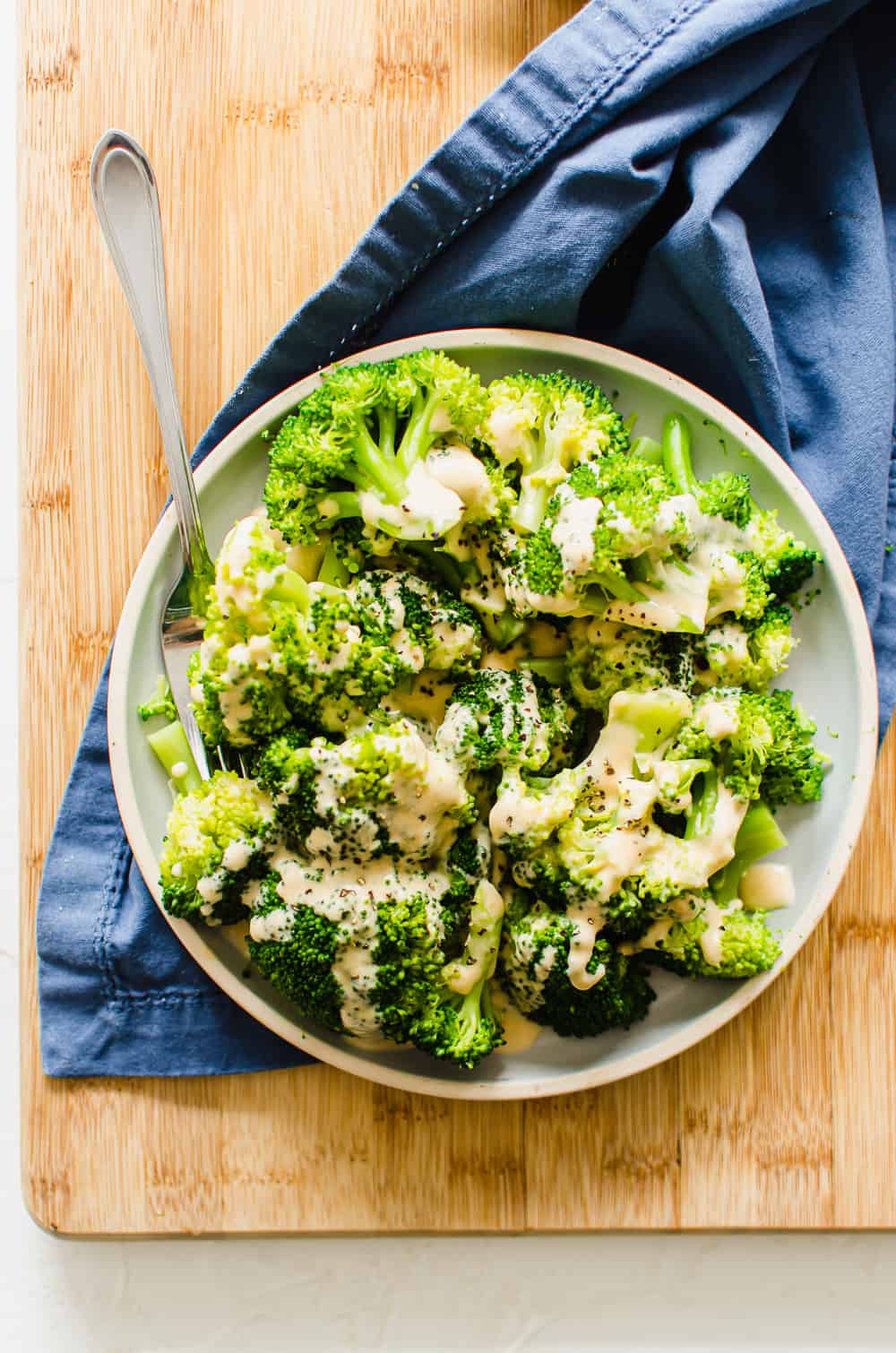 A plate of steamed broccoli with homemade cheese sauce drizzled all over it.