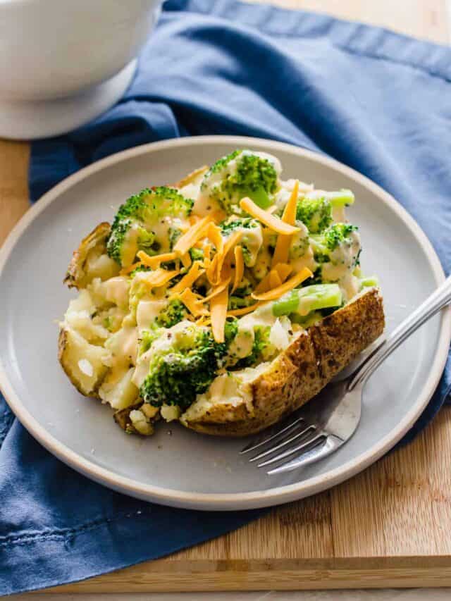 A baked potato cut open and topped with homemade cheese sauce, steamed broccoli, and shredded cheddar cheese.