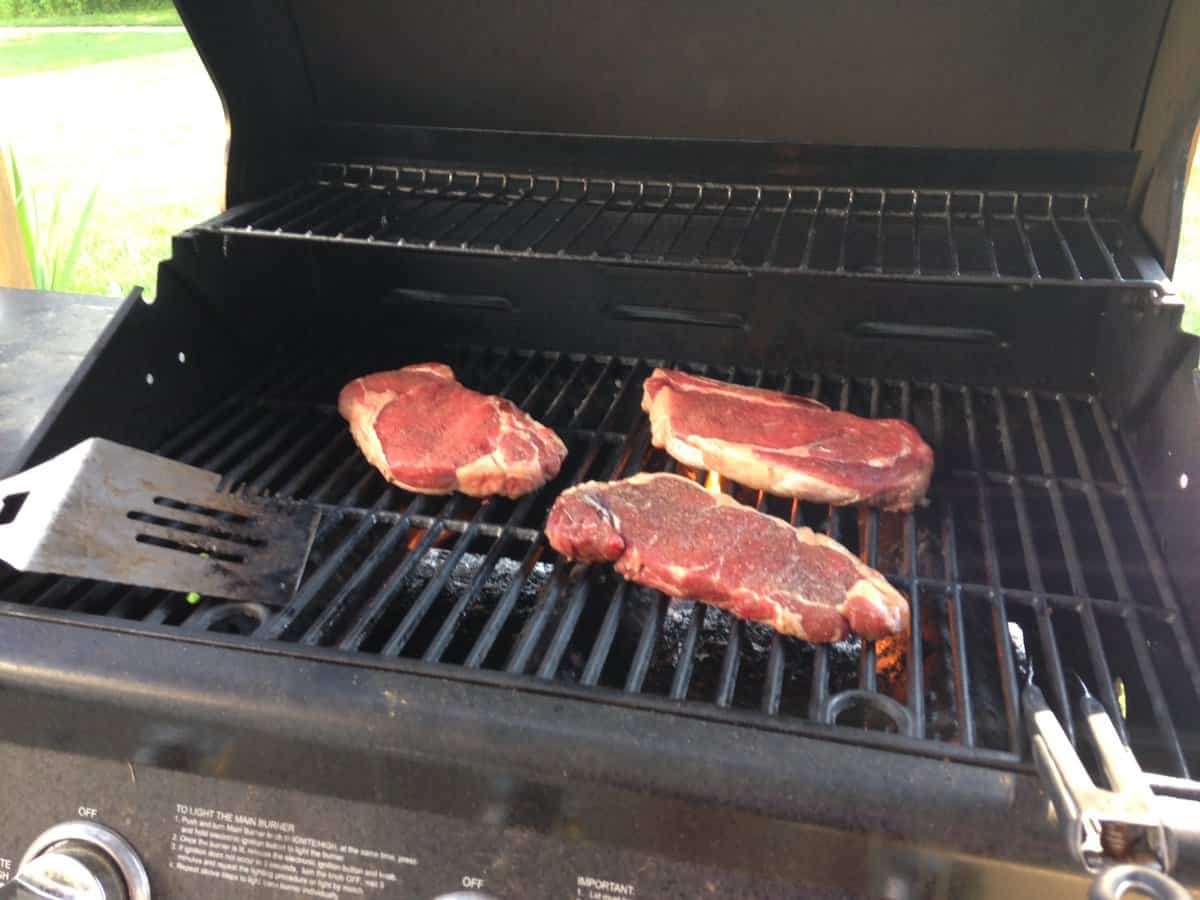 Three raw steaks on a gas grill. 