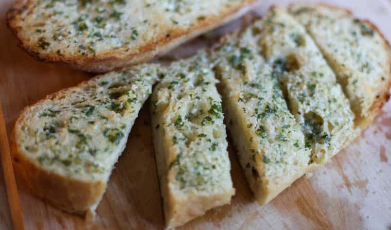 Garlic bread sliced on a wooden cutting board.