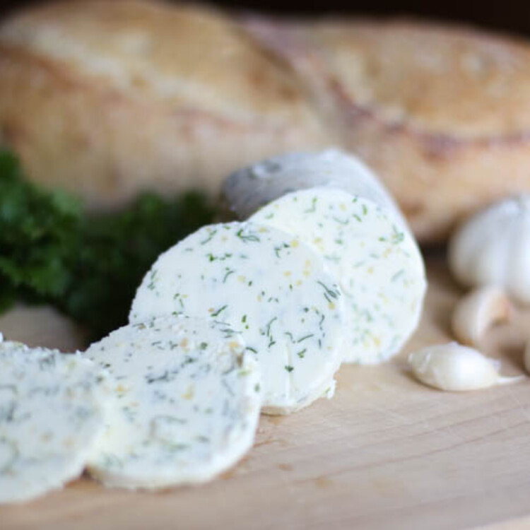 Slices of garlic herb butter with a loaf of bread in the background.