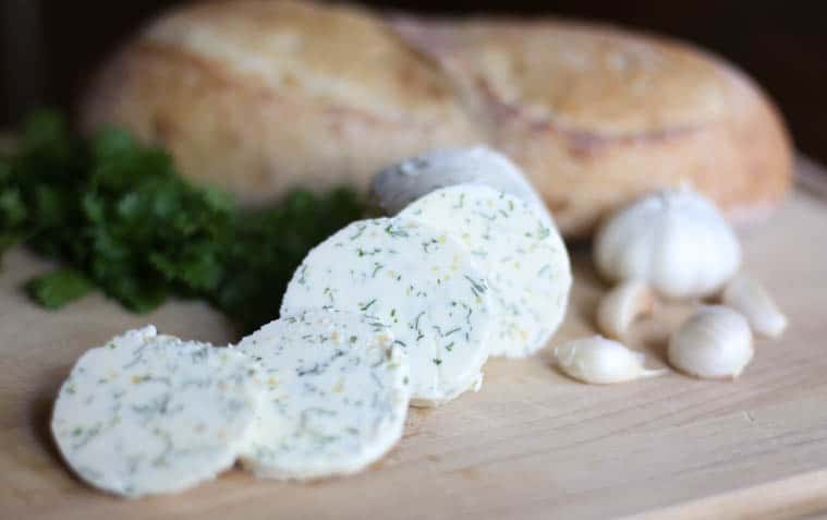 Garlic herb butter sliced on a cutting board with fresh bread in the background.