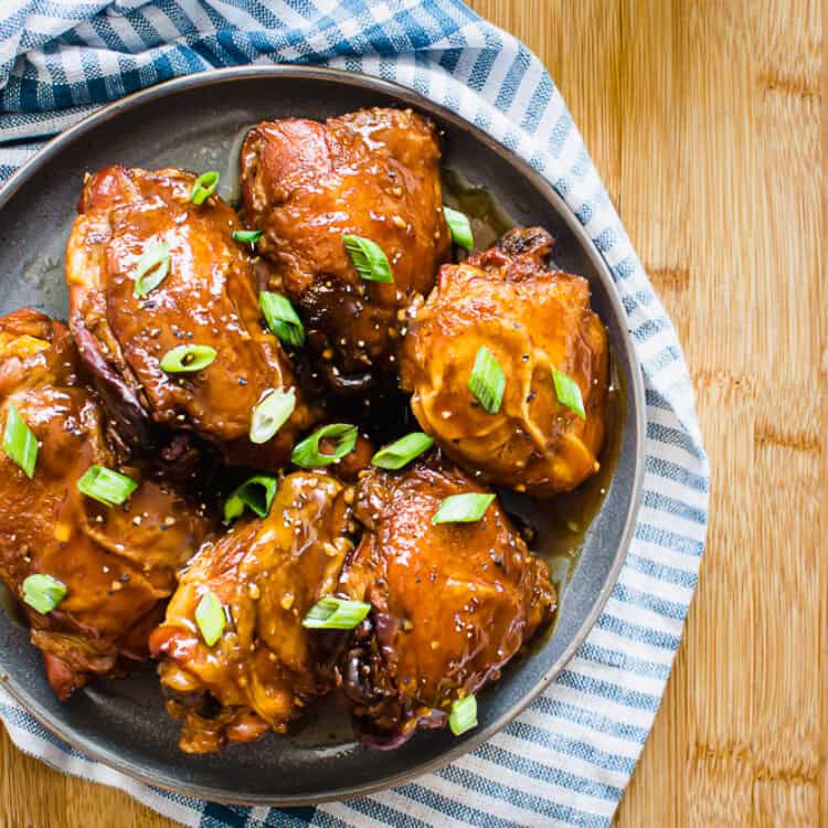 Teriyaki chicken thighs on a grey plate garnished with sliced green onion.