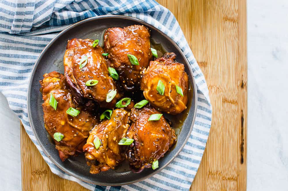 Instant Pot teriyaki chicken thighs on a grey plate garnished with sliced green onion.