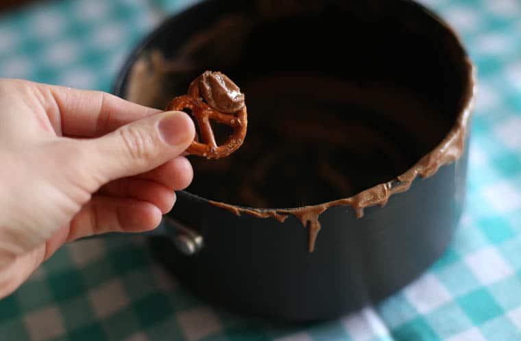 A hand holding a pretzel that scraped the chocolate peanut butter mixture from the puppy chow pan.