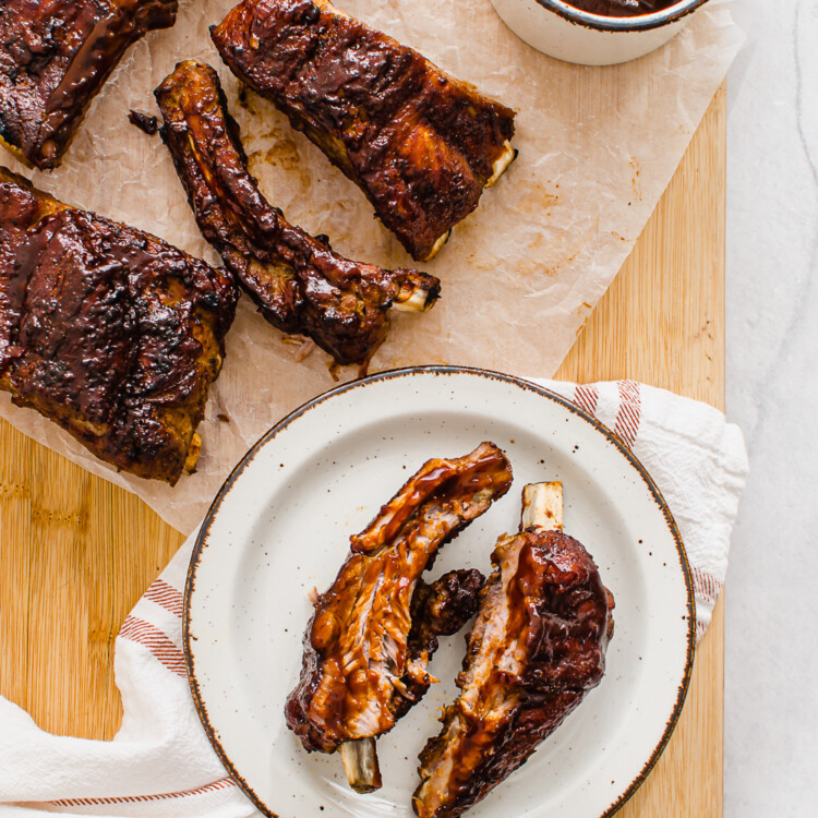 slow cooked ribs on a cutting board with extra sauce on the side
