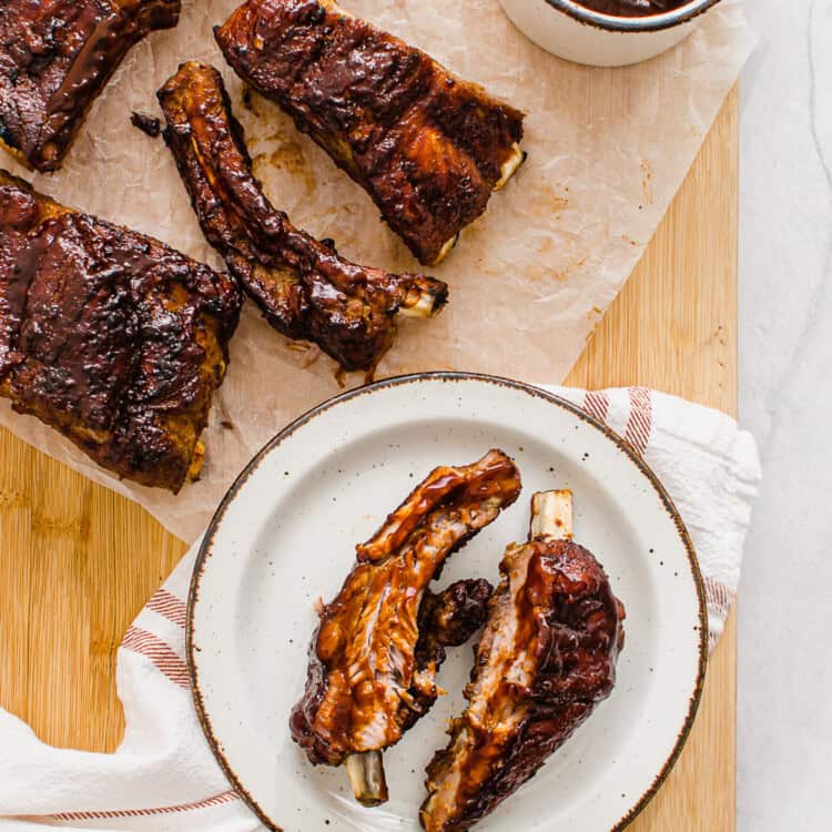 Slow cooked ribs on a cutting board with extra sauce on the side.