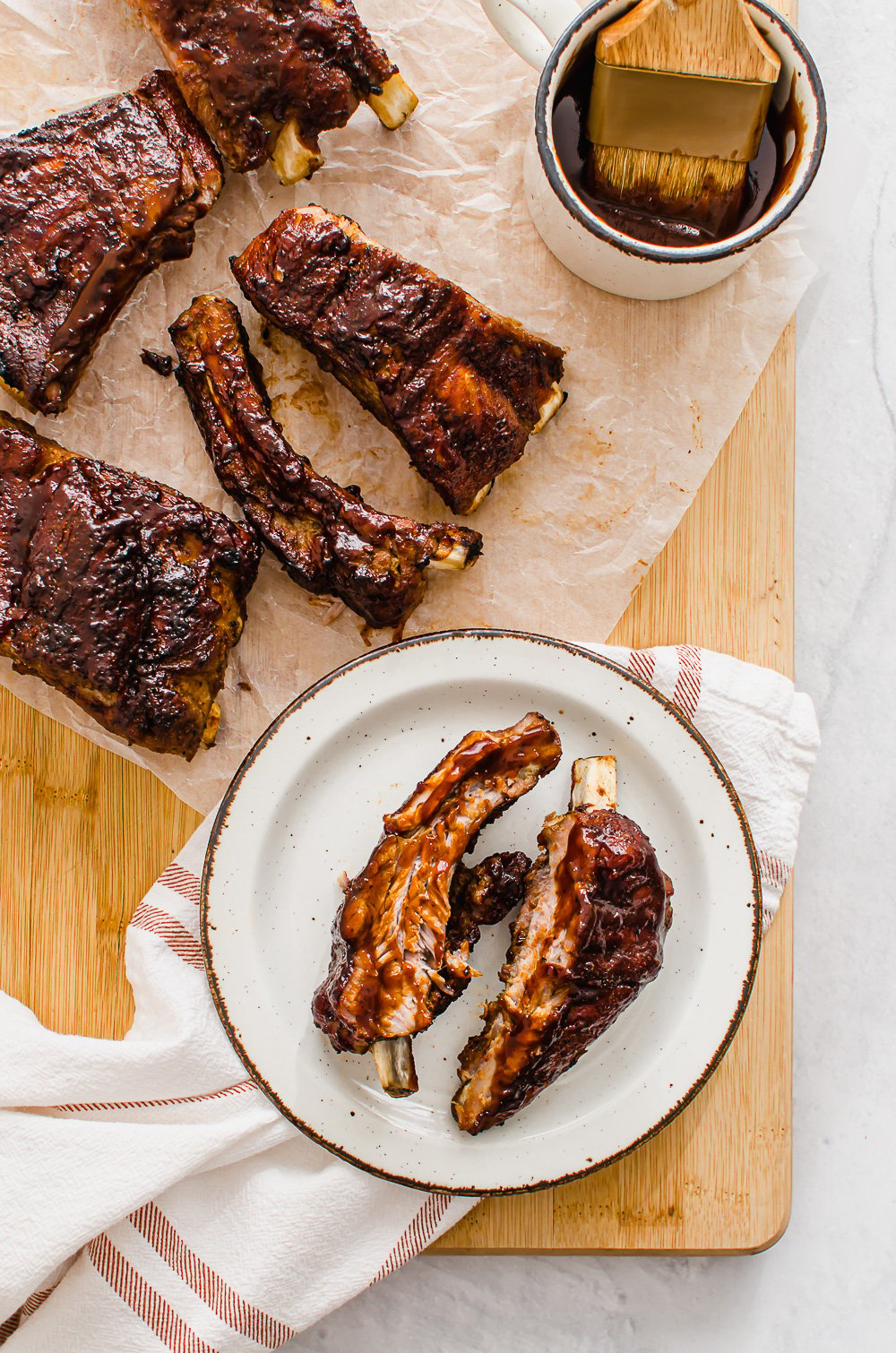 BBQ ribs on a cutting board with extra sauce on the side.