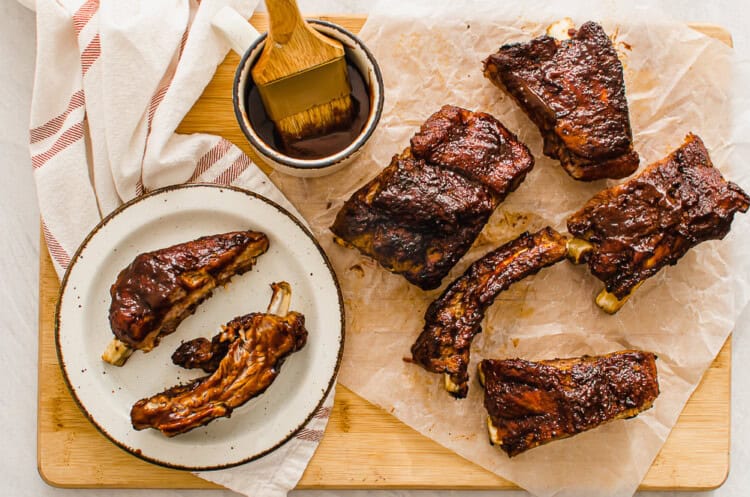 Baby back ribs on a cutting board with extra sauce on the side.