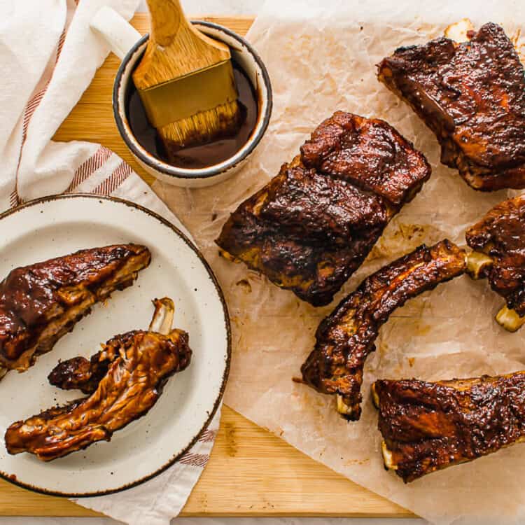 slow cooked ribs on a cutting board with extra sauce on the side