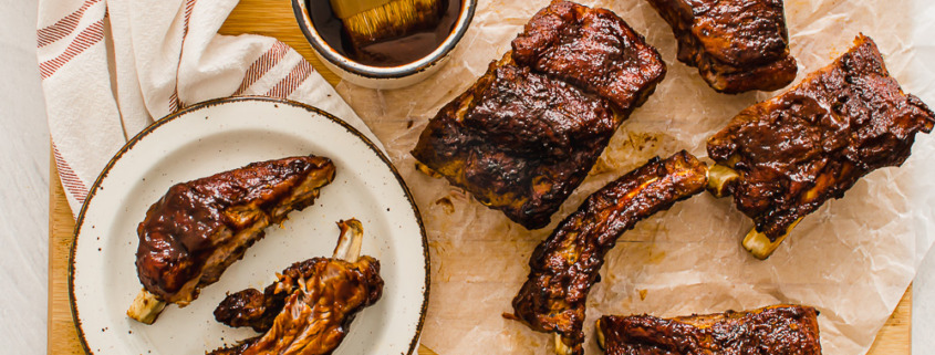 slow cooked ribs on a cutting board with extra sauce on the side