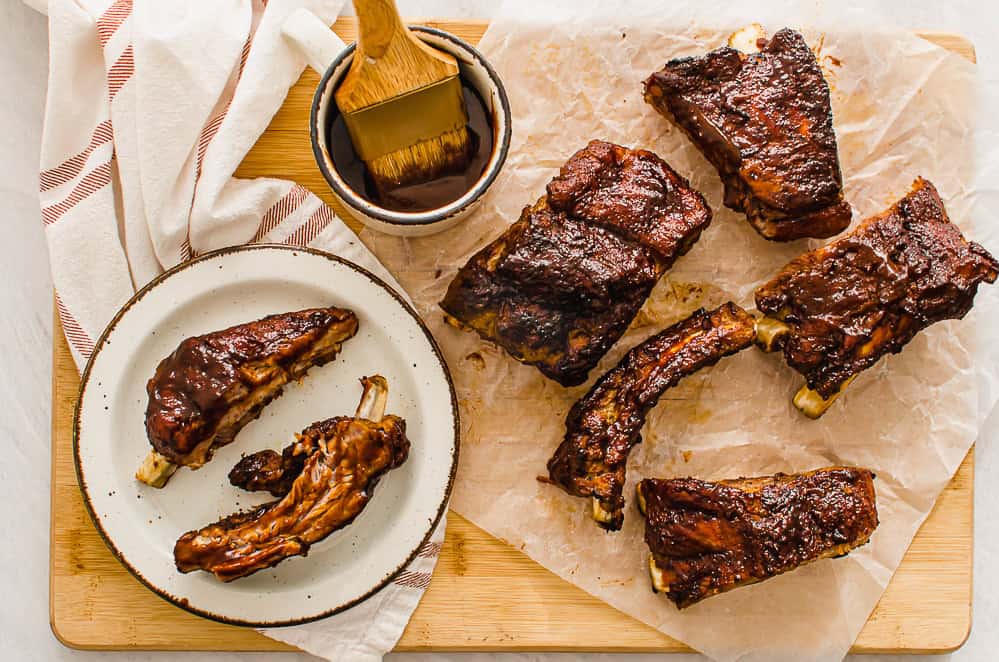 slow cooked ribs on a cutting board with extra sauce on the side.