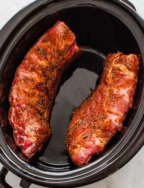 Racks of ribs place along the perimeter of a slow cooker before cooking.