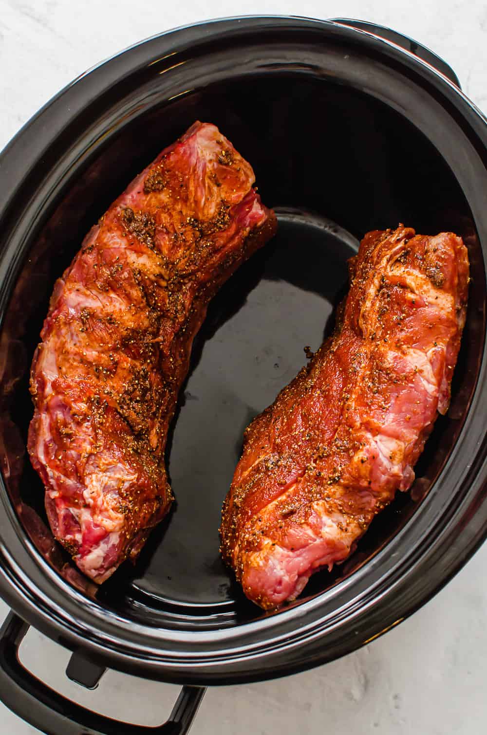 Two seasoned racks of ribs in a crock pot.