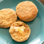 Whole wheat biscuit halves on a plate with butter and honey on top.