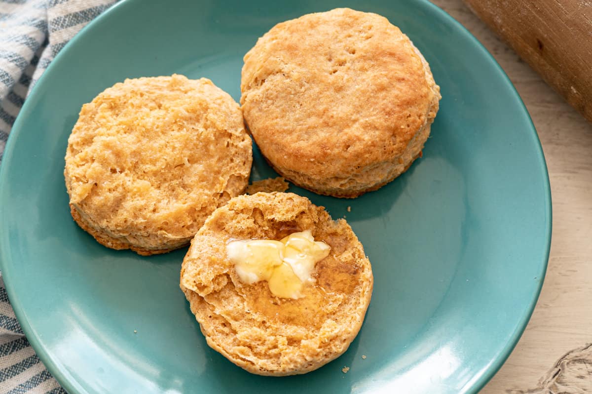 Whole wheat biscuits with butter and honey on top on a plate.