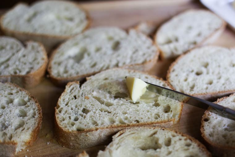 Softened butter being spread out over bread slices to make texas toast. 