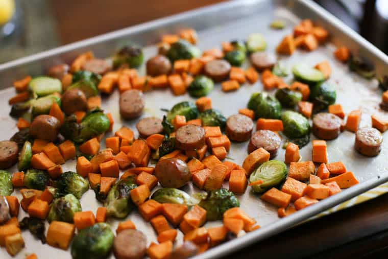 Chicken sausage slices, chopped sweet potatoes, and halved Brussels sprouts spread out on a sheet pan.