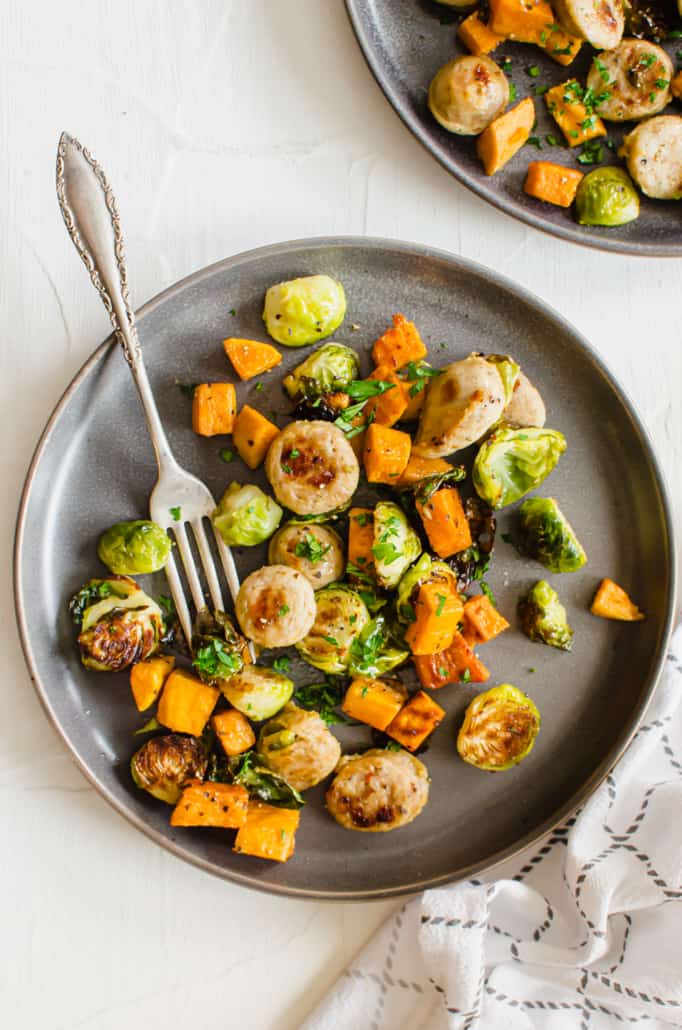 close up of one plate of roasted sheet pan sausage and veggies with a fork