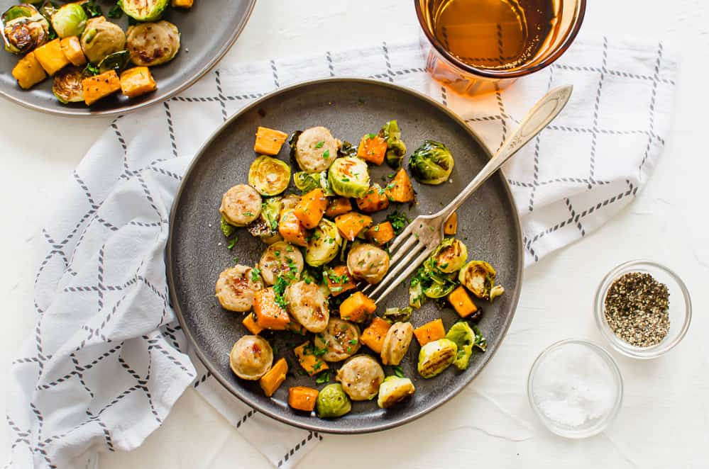 close up of one plate of roasted sheet pan sausage and veggies with a fork.