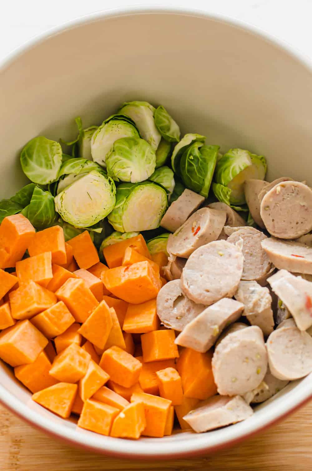 sliced Brussels sprouts, diced sweet potatoes, and sliced chicken sausage in a white bowl.