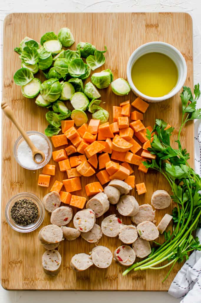 chopped Brussels sprouts, sweet potatoes, and chicken sausage on a large wooden cutting board