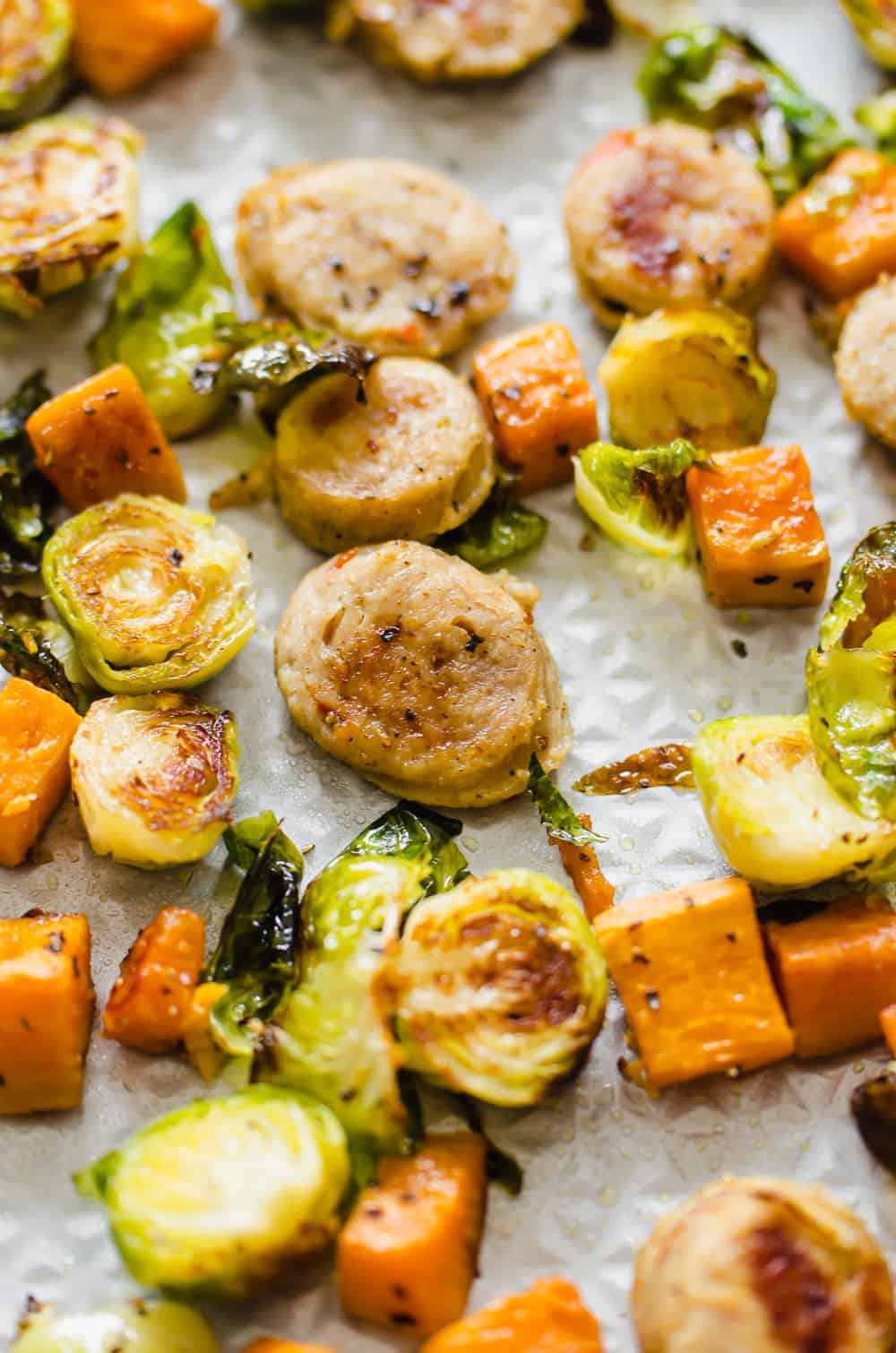 close up shot of roasted chicken sausage and veggies on a sheet pan after coming out of the oven.