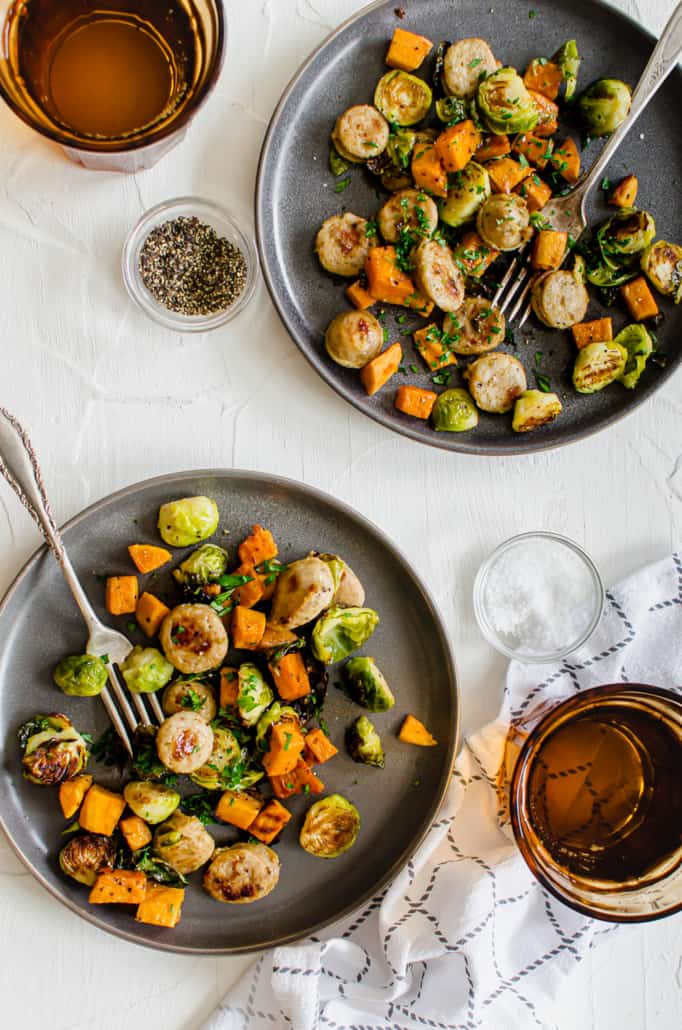 roasted sauges and veggies on two gray plates with a fork, napkin, and drink on the side