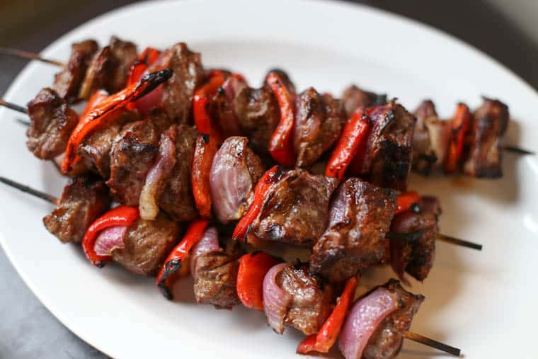 Pile of sirloin steak kabobs on a hite platter.