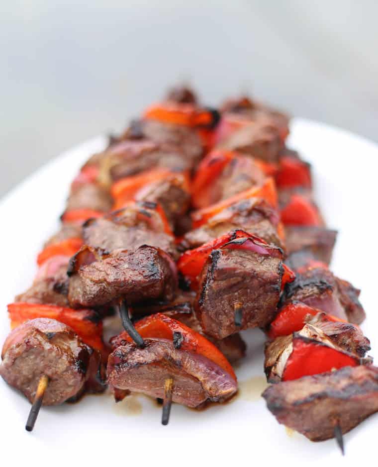 Grilled steak kabobs on skewers stacked on a white platter.