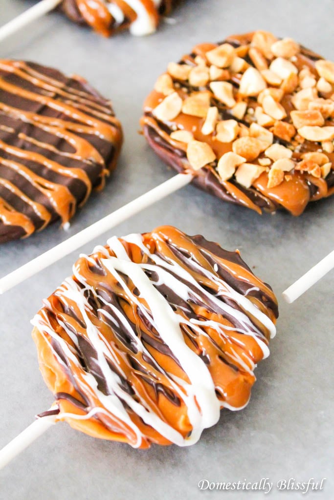 Caramel apple slices on a stick - some with peanuts and others with white icing and caramel drizzle.
