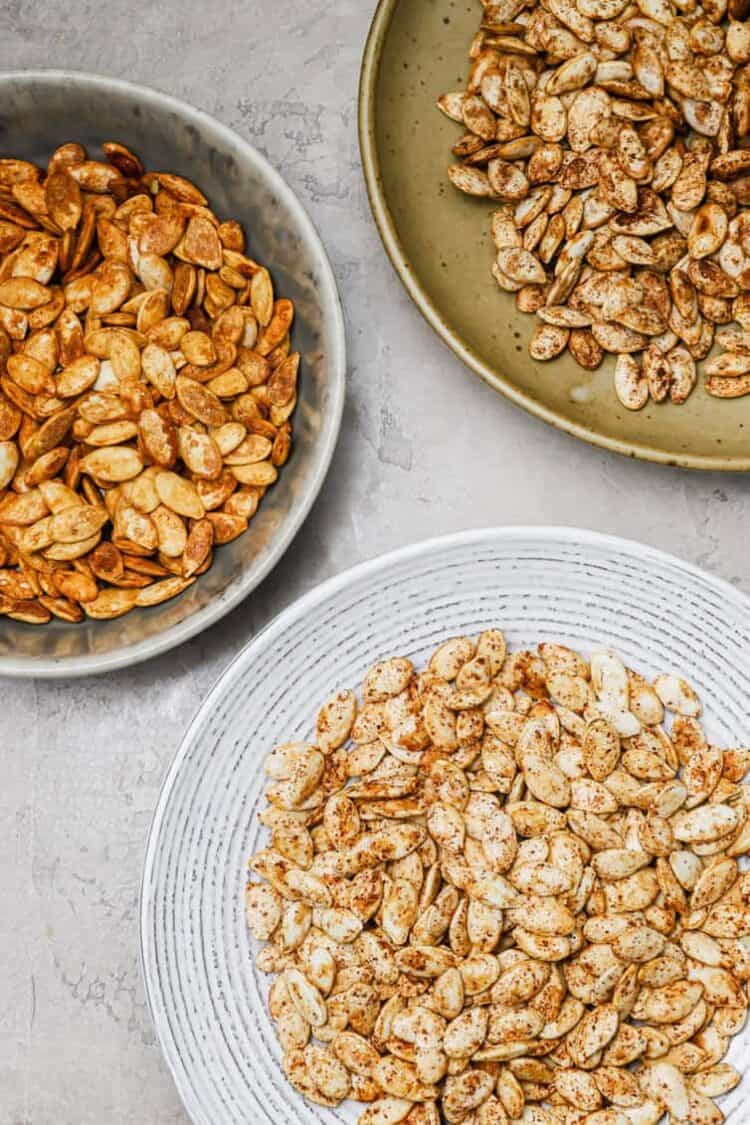 Three different flavors of roasted pumpkin seeds on three different plates.