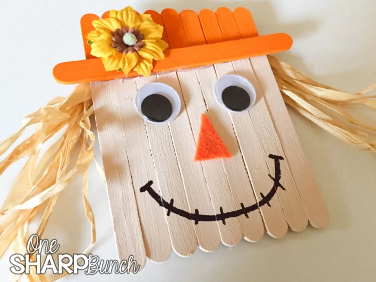 Popsicle sticks glued side by side to look like a scarecrow with the top part painted orange to look like a hat, a black smile drawn on, straw glued on the sides for the hair, and an orange triangle glued on as the nose.
