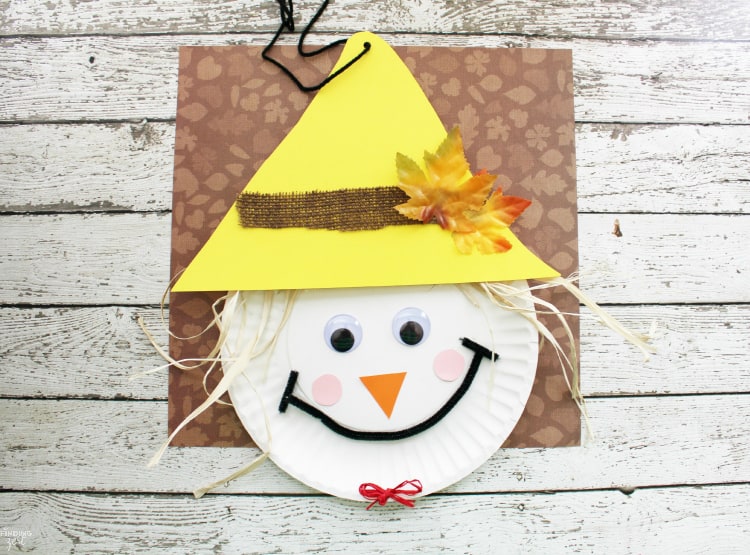 A paper plate with a yellow triangle hat with straw hair, google eyes, pipe cleaner mouth, and construction paper for a nose and cheeks.