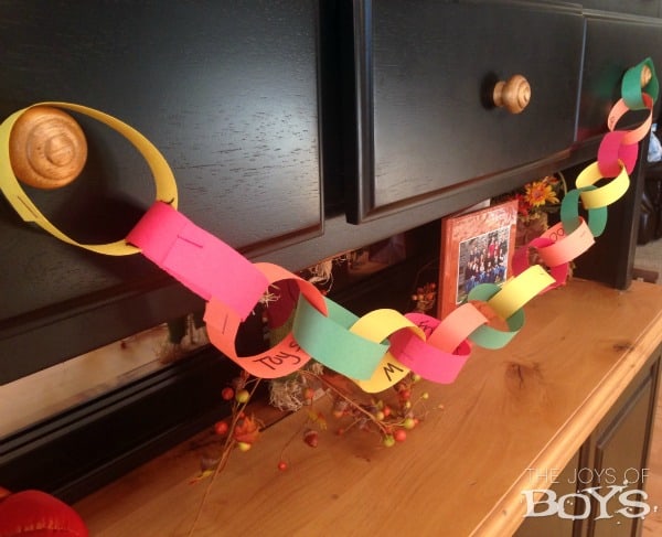 A multi-colored paper chain with thankful statements written on each on hanging on a dresser.