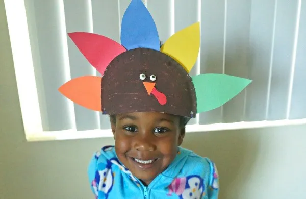 Small child with a homemade paper plate turkey hat.