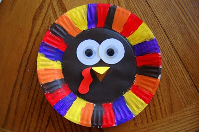 A paper plate painted brown in the middle and different colors all around the edge and with google eyes and a construction paper beak.