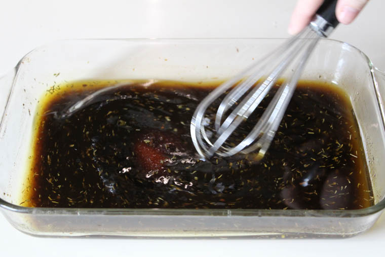 A hand whisking together the ingredients of cranberry balsamic chicken in a clear baking dish.