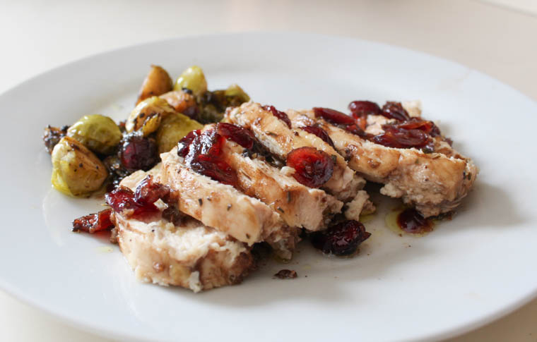 Cranberry balsamic chicken breast sliced on a plate with dried cranberries on top and chopped Brussels sprouts.
