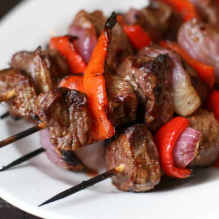 Grilled steak kabobs on a white platter.