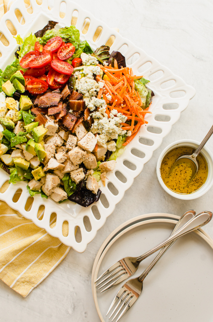 cobb salad on a white plate with yellow napkin and dressing on the side