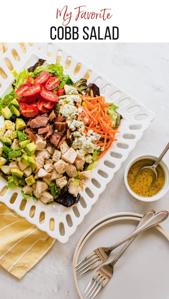 cobb salad on a white plate with yellow napkin and dressing on the side