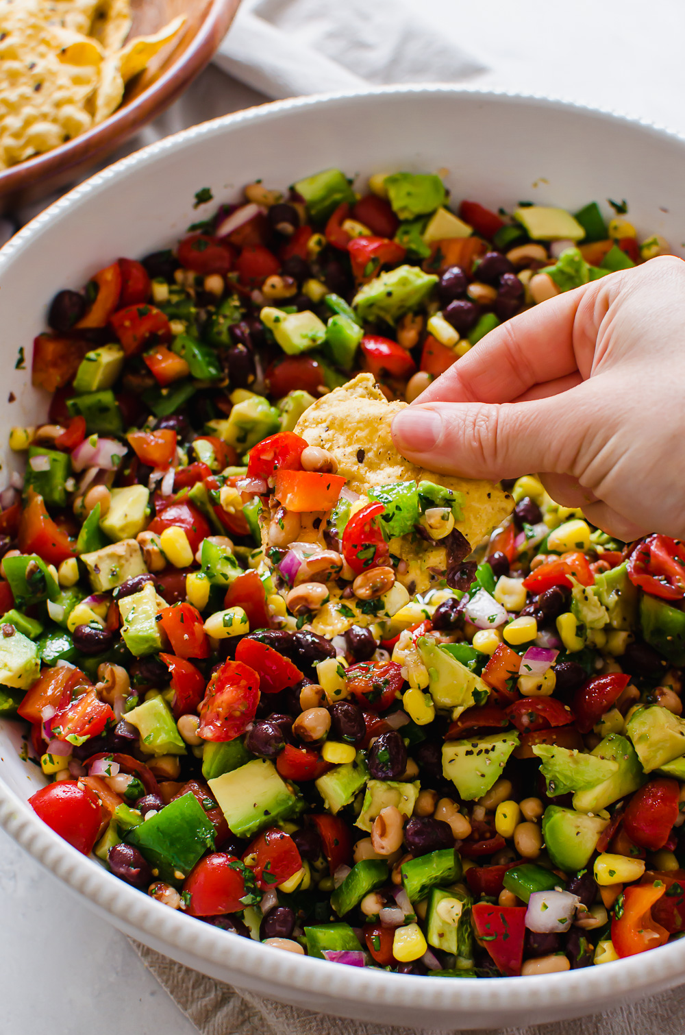Fiesta chopped salad in a white bowl with a hand dipping in with a chip.