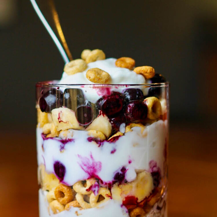 Breakfast Cereal Parfait in a glass with layers of Greek yogurt, blueberries, and Cheerios.