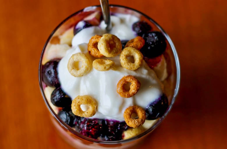 Looking into the top of a glass that has layers of Greek yogurt, blueberries, and multi-grain Cheerios in it to make a Breakfast Cereal Parfait.