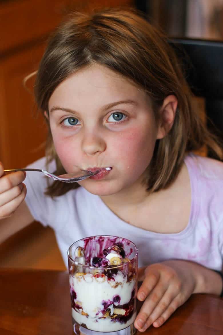 A young girl eating a breakfast cereal parfait made of Greek yogurt, blueberries, bananas, and multi-grain Cheerios.