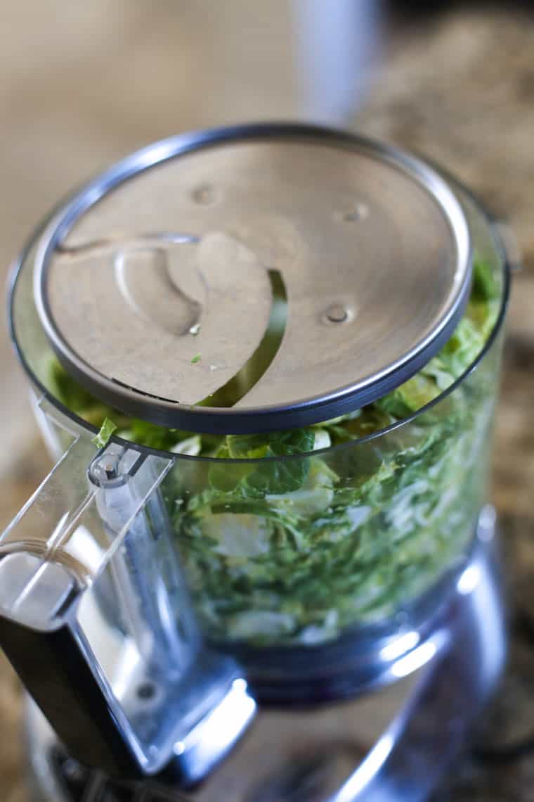 Food processor full of shaved Brussels sprouts with slicing tool on top.