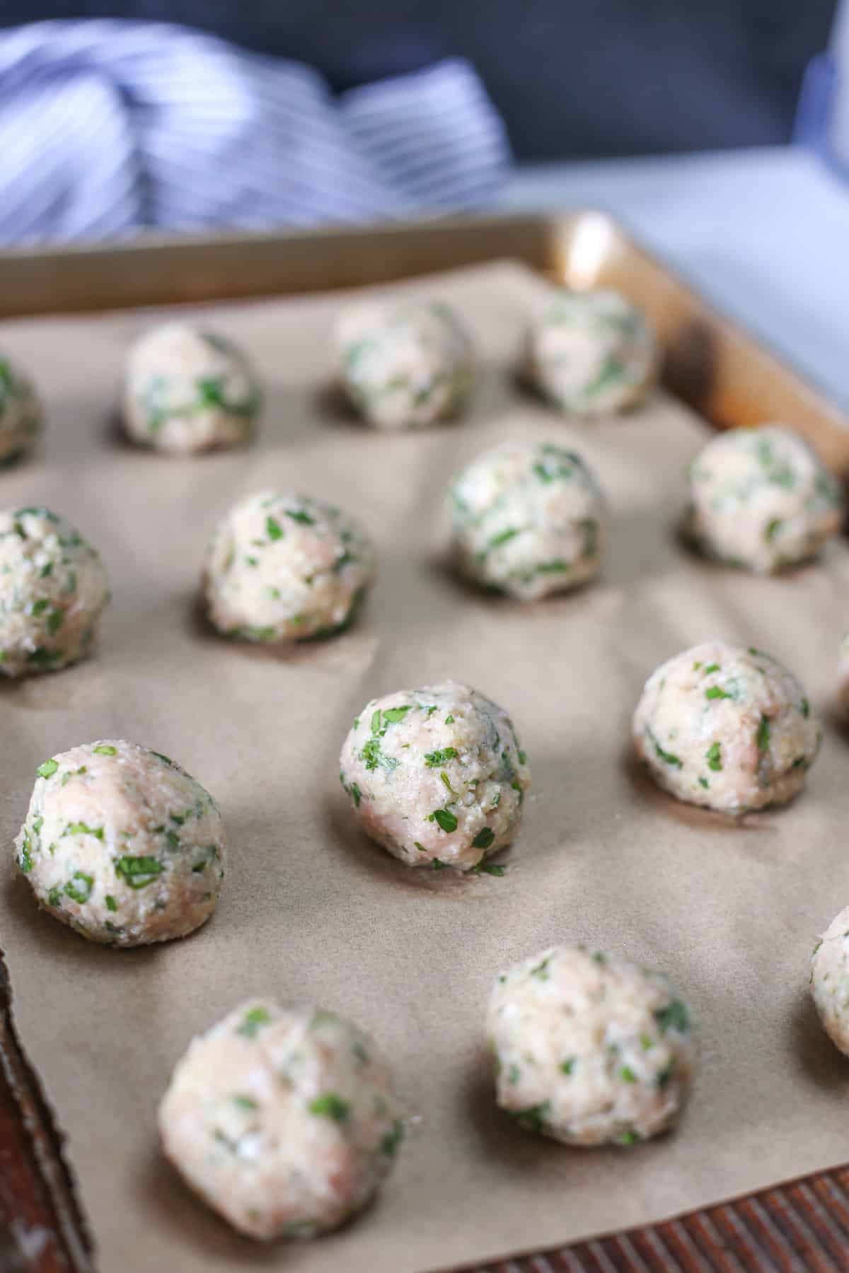 Raw, rolled meatballs on a sheet pan.